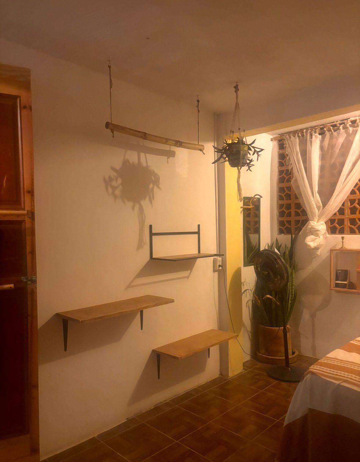 Ein Zimmer mit einem Bett, einer Zimmerpflanze, einem Ventilator und Regalen an der Wand.