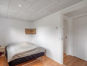 Une chambre à coucher avec un lit, une étagère fixée au mur et une porte donnant sur une autre pièce.