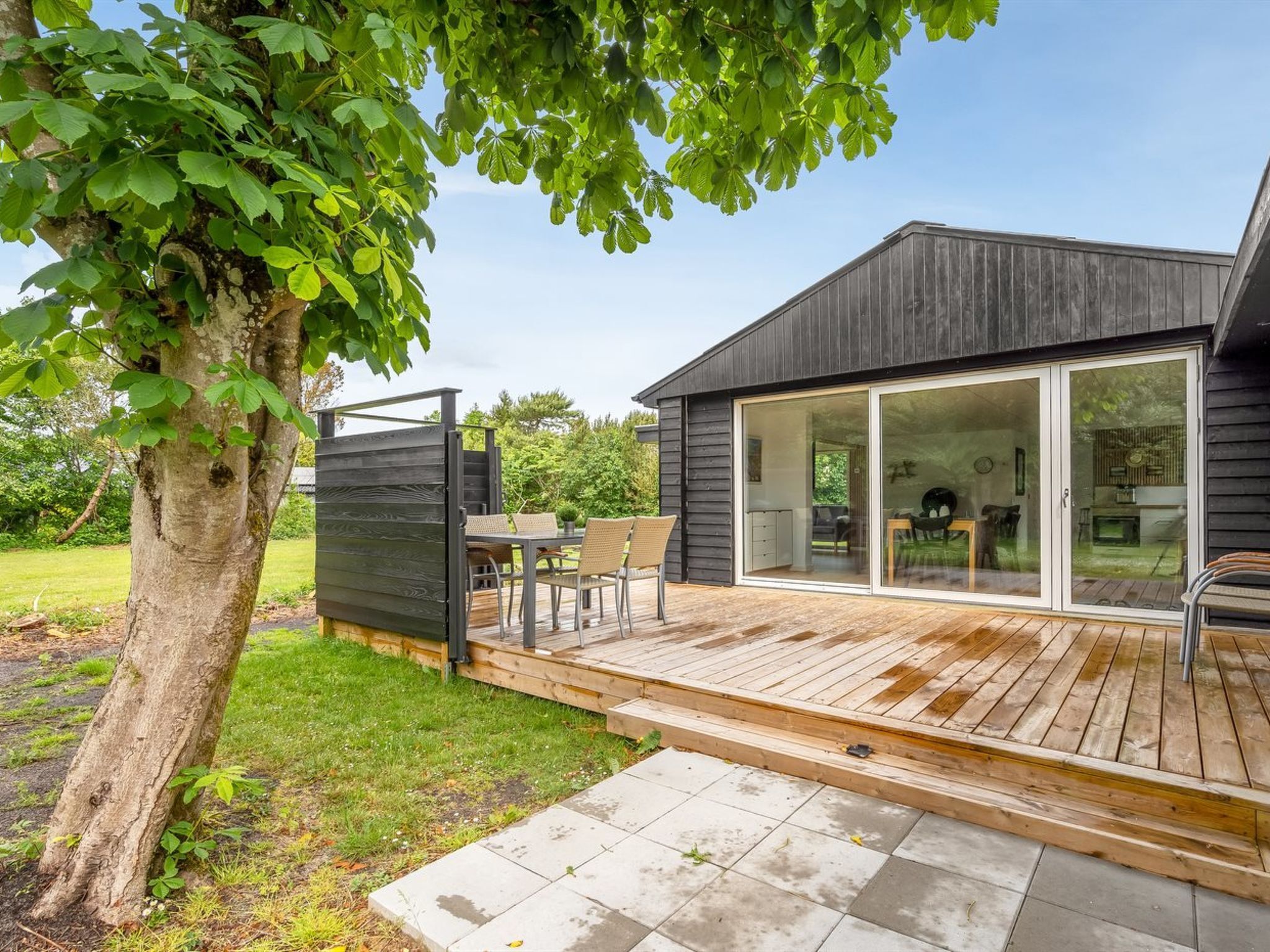 Een modern huis met een terras, een eethoek en een grote schuifpui die naar een binnenruimte leidt.