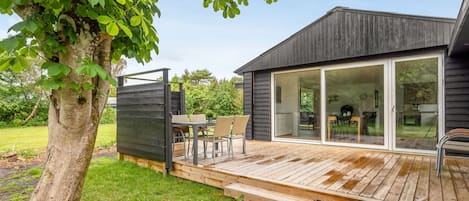 A modern house with a deck, a dining area, and a large sliding glass door leading to an interior space.