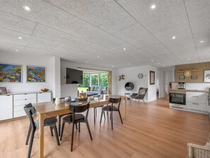 Une cuisine spacieuse équipée d’appareils modernes, un coin repas avec une table et des chaises en bois, et un salon avec un canapé et un téléviseur.