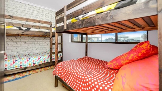A bunk bed room with a white brick wall, a window with a view, and a red polka dot bedspread. - NR 4 Cove Apartment Carrickalinga (Carrickalinga)