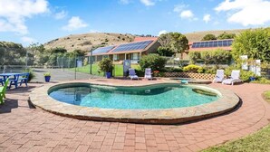 A swimming pool with a brick border, surrounded by lounge chairs and a fenced area with solar panels. - NR 4 Cove Apartment Carrickalinga (Carrickalinga)