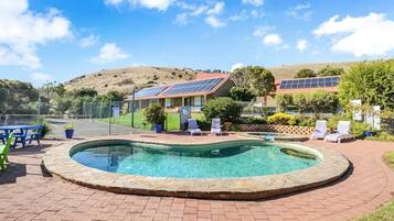 A swimming pool with a brick border, surrounded by lounge chairs and a fenced area with solar panels.