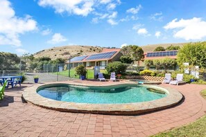 A swimming pool with a brick border, surrounded by lounge chairs and a fenced area with solar panels. - NR 4 Cove Apartment Carrickalinga (Carrickalinga)