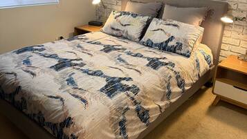 A bedroom with a bed, a nightstand, a lamp, a window, and a wall with a textured pattern.