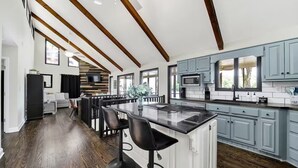 A modern kitchen with a central island, bar stools, and a dining area with a sofa and TV.