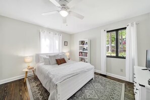 A bedroom with a bed, a nightstand, a bookshelf, a window with curtains, and a ceiling fan.