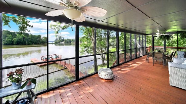 A covered deck with a view of a lake, a ceiling fan, and outdoor furniture.