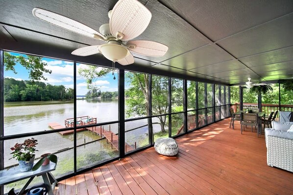 A covered deck with a view of a lake, a ceiling fan, and outdoor furniture.