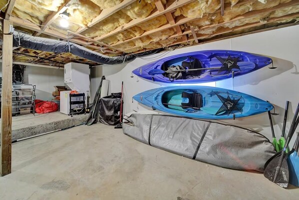 A basement with two kayaks, a red bag, and a kayak stand.