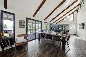 A modern kitchen with dark wooden floors, a dining area with a large table, and a view of a deck through glass doors.