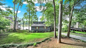 A residential property with a well-maintained lawn, a house with a dark exterior, and a dock extending into a body of water.