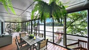 A covered outdoor area with a table and chairs, a hanging fern, and a view of a lake.