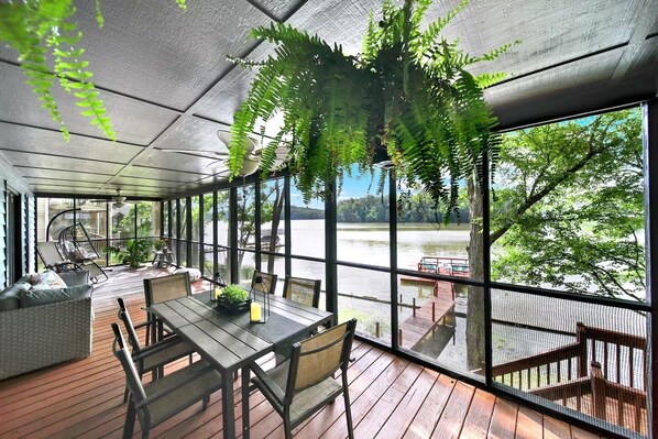 A covered outdoor area with a table and chairs, a hanging fern, and a view of a lake.
