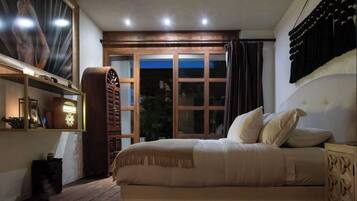 Un dormitorio con cama, mesita de noche, aparador de madera, ventana con cortinas y lámpara fijada a la pared.