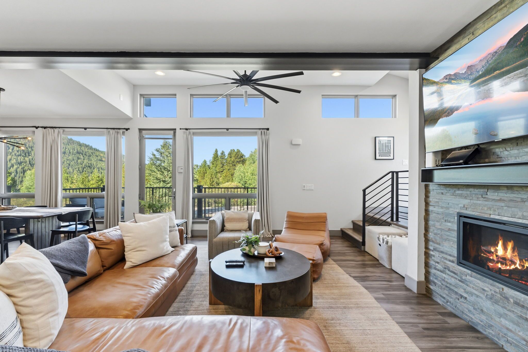 A spacious living area with a fireplace, leather sofas, a coffee table, and large windows offering a view of the outdoors.