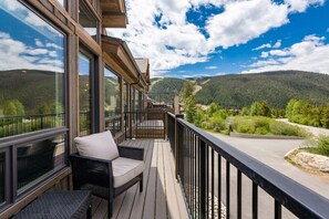 Ein Balkon mit Blick auf eine bewaldete Bergkette, ausgestattet mit Korbstühlen und einem Tisch.