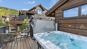 Een houten terras met een jacuzzi, stoelen en uitzicht op een berg.