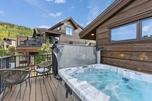 Eine Holzterrasse mit Whirlpool, Stühlen und Blick auf einen Berg.