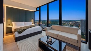 Ein modernes Schlafzimmer mit einem großen Bett, einer Couch und Blick auf die Stadt durch große Fenster.