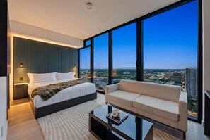 Ein modernes Schlafzimmer mit einem großen Bett, einer Couch und Blick auf die Stadt durch große Fenster.