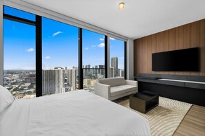 Een moderne hotelkamer met een groot bed, een zithoek, een flatscreen televisie en uitzicht op de stad.