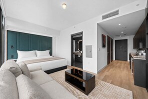 Ein modernes Hotelzimmer mit einem großen Bett, einer Sitzecke, einem Glastisch und einer Küchenzeile.