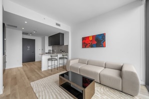 Ein modernes Wohnzimmer mit einer Couch, einem Couchtisch und einer Küchenzeile im Hintergrund.
