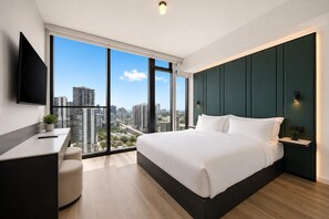 Ein modernes Hotelzimmer mit einem großen Bett, einem Schreibtisch und Blick auf die Skyline durch raumhohe Fenster.