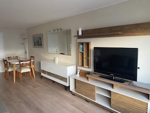 A modern living room with a flat-screen TV, wooden furniture, a white console, and a dining area with chairs. - Torre de las Américas Apartment, Punta del Este (Punta del Este)