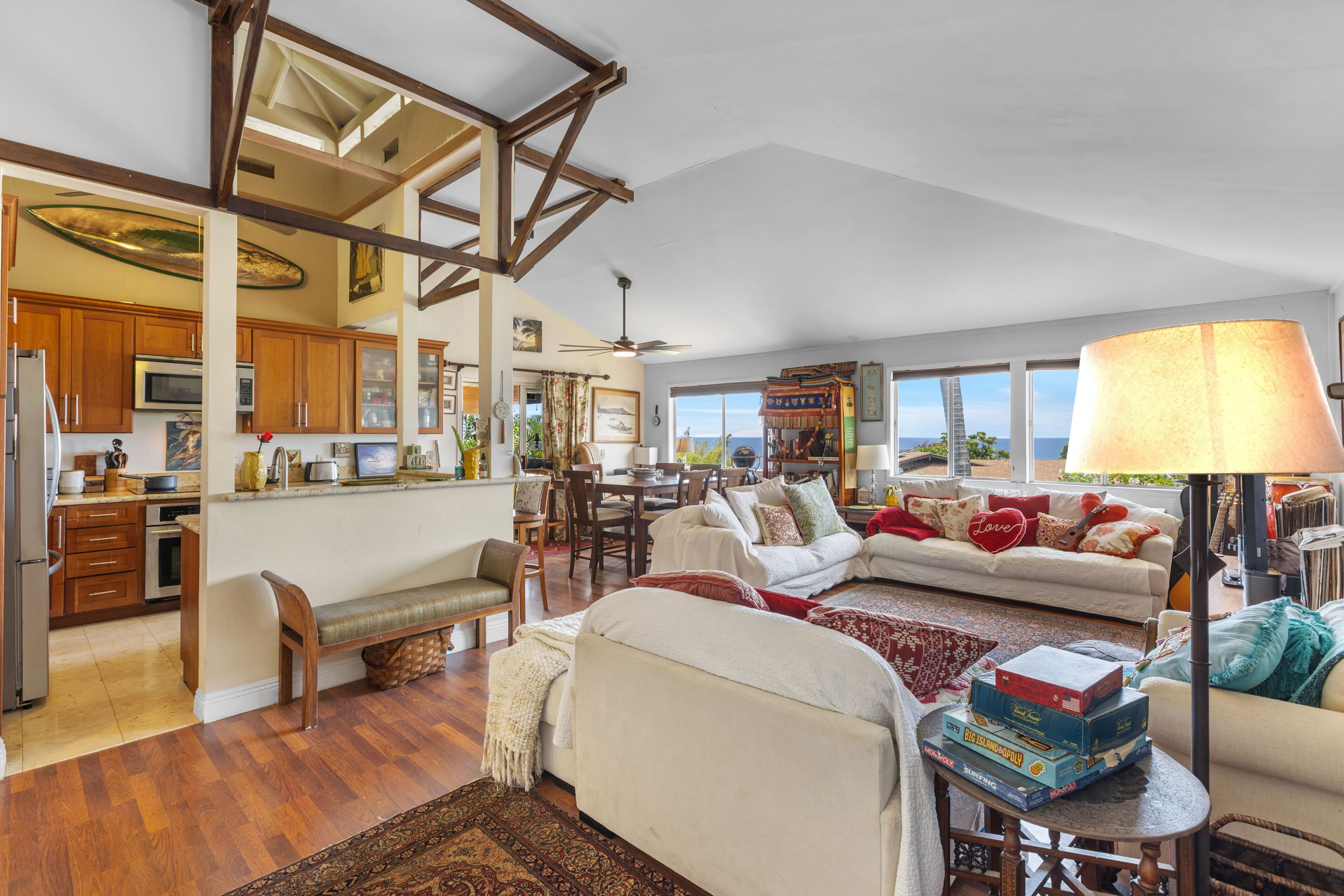 A spacious living area with a high ceiling, wooden beams, a dining area, and a view through large windows.