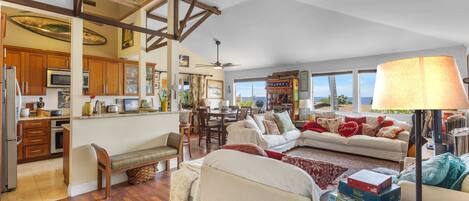 A spacious living area with a high ceiling, wooden beams, a dining area, and a view through large windows.