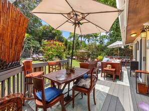 Eine Terrasse im Freien mit Holzmöbeln, darunter Tische und Stühle, und einem großen Sonnenschirm, der Schatten spendet.