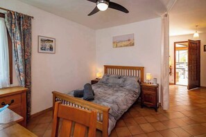 A bedroom with a bed, a wooden nightstand, a desk, a chair, a ceiling fan, and a door leading to another room. - Villa Sleeps 12 with Outdoor Pool (Laroque-Des-Albères)