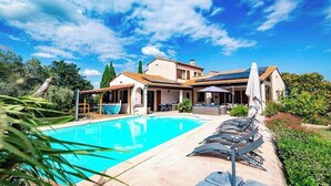 Uma área junto à piscina com espreguiçadeiras, piscina e um edifício com telhado ladrilhado.