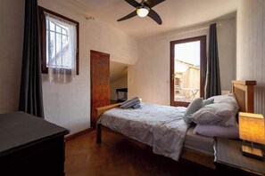 Ein Schlafzimmer mit Bett, Schreibtisch, Deckenventilator und einem Fenster mit Vorhängen.
