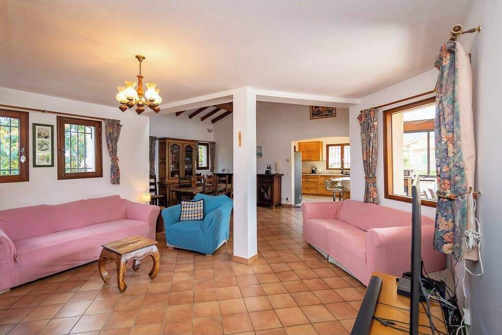 A living room with two sofas, a coffee table, and a chandelier. There is a kitchen visible in the background.