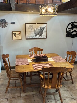 Een houten eettafel met zes stoelen, een lijst met een afbeelding van een stier, en een wandlamp.