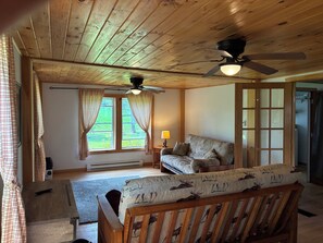 A room with a wooden ceiling, a ceiling fan, a sofa, a window with curtains, and a lamp. - Rustic, serene 2-bedroom house in Constableville. (Constableville)