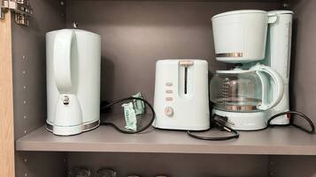 A kitchen with a coffee maker, toaster, and a scale. There are also several glass containers on the shelf below.