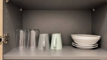 A kitchen shelf with clear glasses, a white pitcher, and stacked white plates.