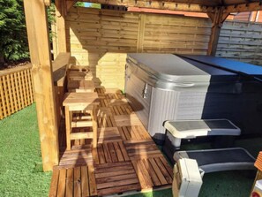 A hot tub area with a wooden deck, a hot tub, and a small table. - Cabin Sleeps 4 with Hot Tub and Parking (York)