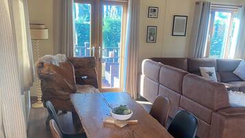A spacious living area with a wooden dining table, a sofa, and a balcony with curtains.