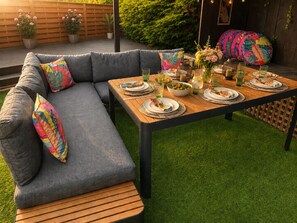 A dining area with a wooden table set for a meal, a grey sofa with colorful cushions, and a small round table with a single chair. - Cabin Sleeps 4 with Hot Tub and Parking (York)