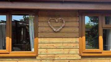 A wooden cabin with a heart-shaped decoration on the wall, large windows, and a visible roof.