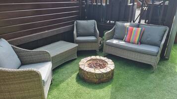 A patio area with wicker furniture and a stone fire pit.