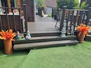 Eine Holzterrasse mit Treppen zu einem überdachten Bereich, Gartenmöbeln und dekorativen Statuen.