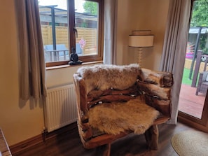 A room with a wooden chair covered in fur, a window with curtains, a radiator, and a lamp. - Cabin Sleeps 4 with Hot Tub and Parking (York)