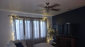 A living room with a ceiling fan, a sofa, a television, and a plant with lights. - Spacious 4-bedroom house in lovely Bakersfield with AC (Bakersfield)